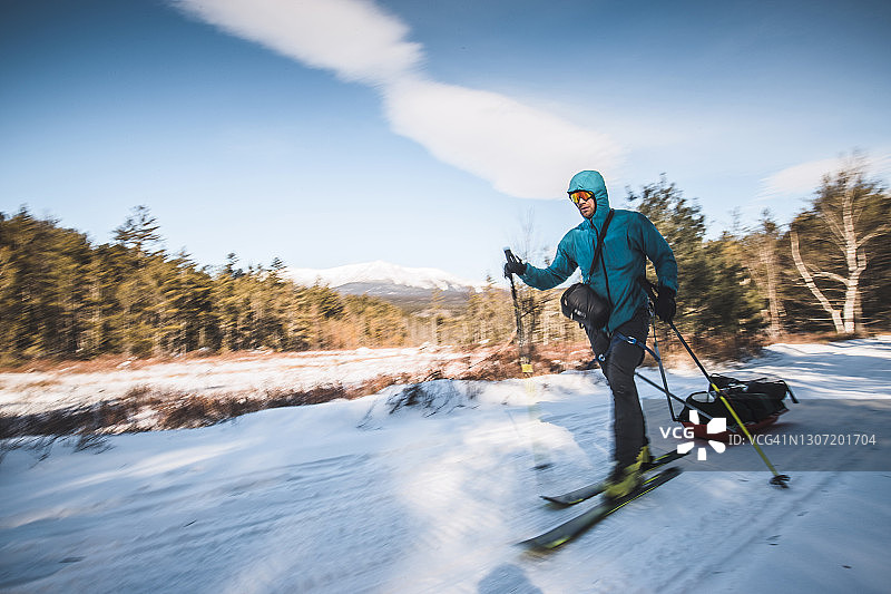 男子在缅因州卡塔丁雪地小路上滑雪，拖着雪橇图片素材