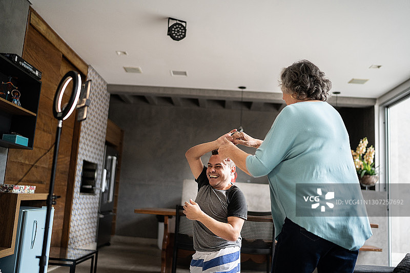患有侏儒症的年轻男人和他的母亲在家跳舞并录制视频图片素材