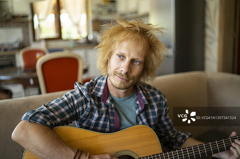 坐在沙发上弹吉他的年轻帅气男人图片素材