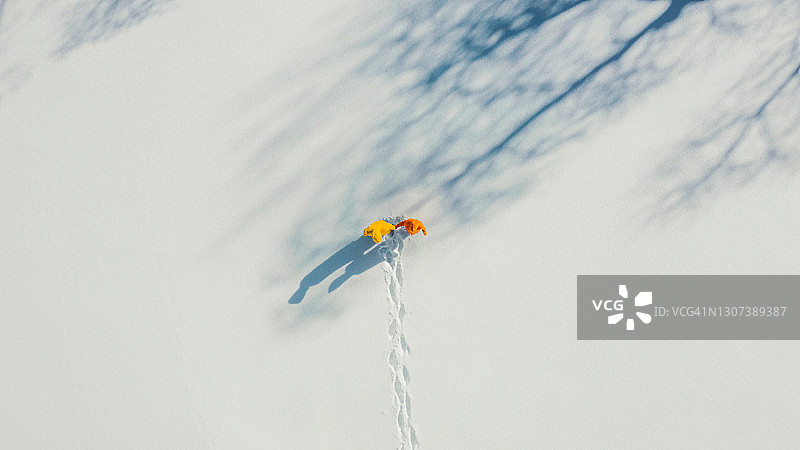 航拍：阳光明媚的日子里，一对身穿黄色和橙色雨衣的年轻夫妇在雪地里行走图片素材