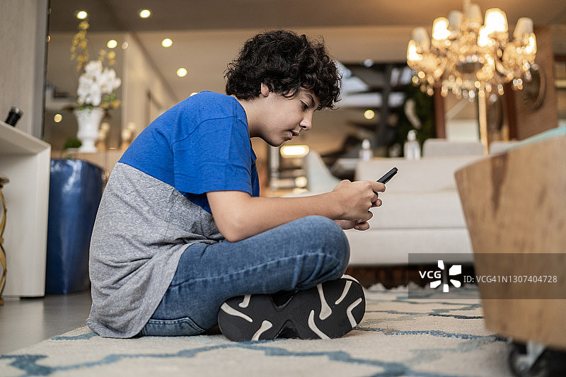 男孩坐在家里地板上玩手机图片素材
