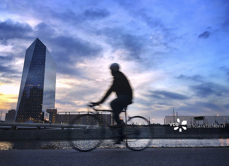 骑行者在斯库基尔河畔小径的日落时分，欣赏城市天际线图片素材