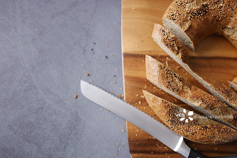 深灰色背景木制砧板上的芝麻黑孜然百吉饼切片图片素材