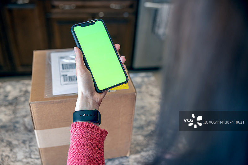 女人手持色度键绿屏手机扫描标签并退回包裹特写图片素材