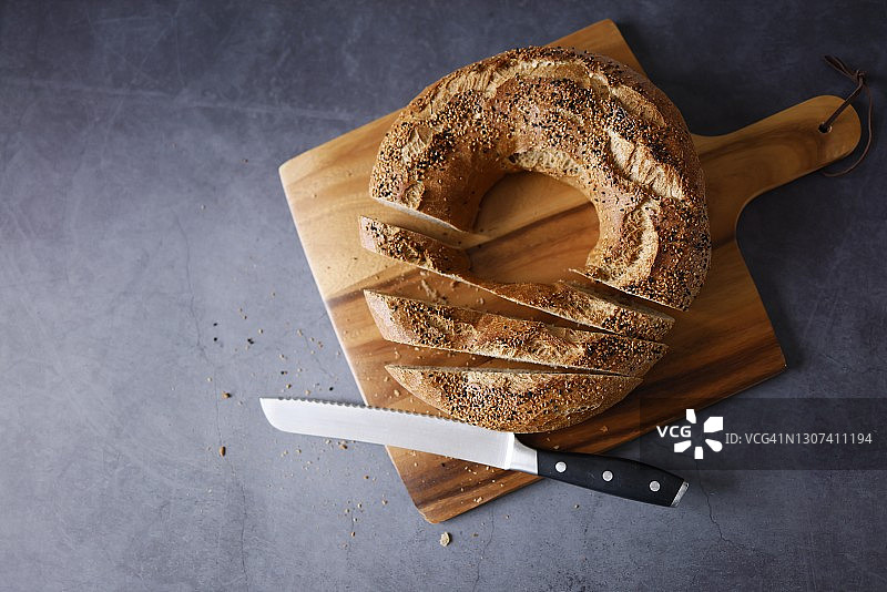 深灰色背景木制砧板上的芝麻黑孜然百吉饼切片图片素材