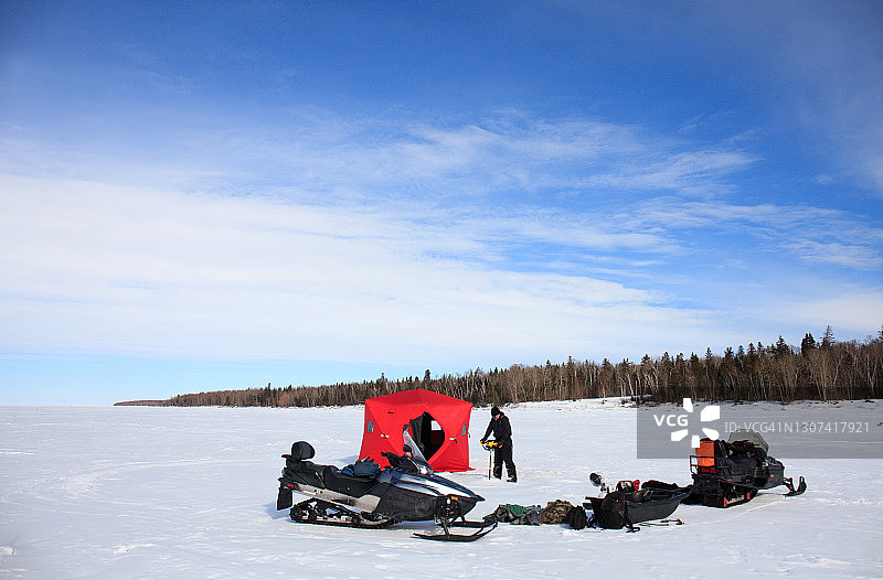 在加拿大马尼托巴省，男人用螺旋钻在冰上钻孔进行冰钓图片素材
