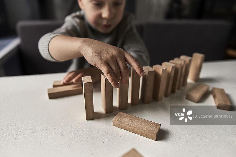 专注的男孩坐在桌旁玩木制玩具积木图片素材
