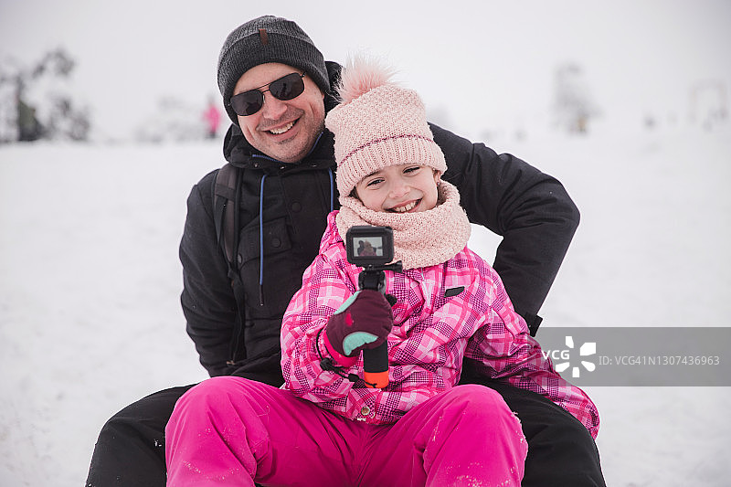 女孩用GoPro相机和父亲一起玩雪橇自拍图片素材