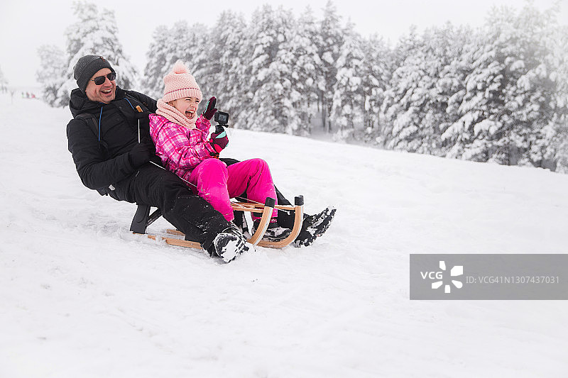 兴奋的女孩和爸爸一起玩雪橇，拿着GoPro图片素材