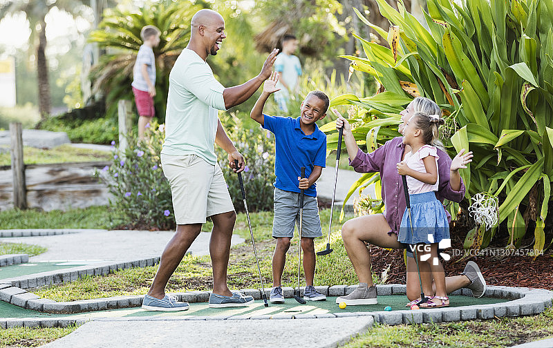 跨种族家庭，两个孩子在玩迷你高尔夫图片素材