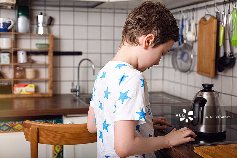 男孩把水壶放在厨房的炉子上烧水图片素材