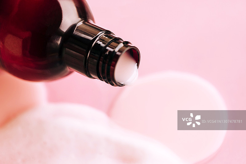 琥珀色玻璃瓶中倒出的淋浴露在粉红色背景上。年度潮流产品。健康概念图片素材