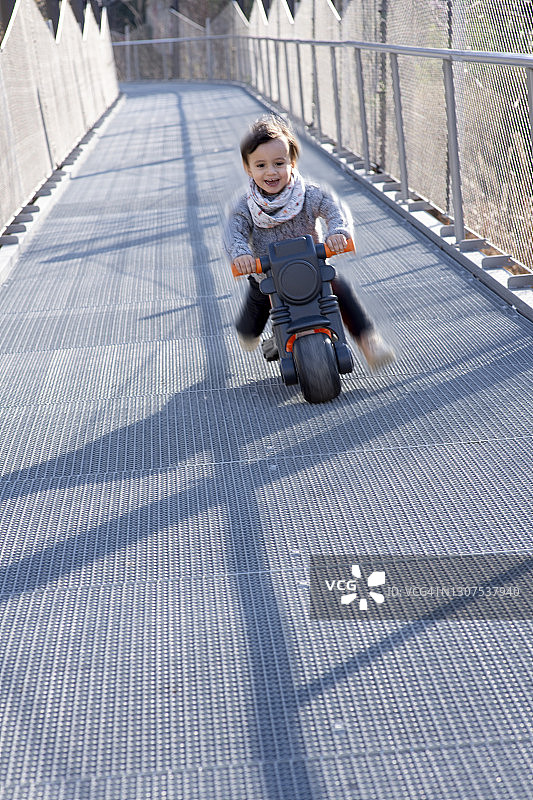 小男孩骑着塑料摩托车从金属斜坡上滑下图片素材