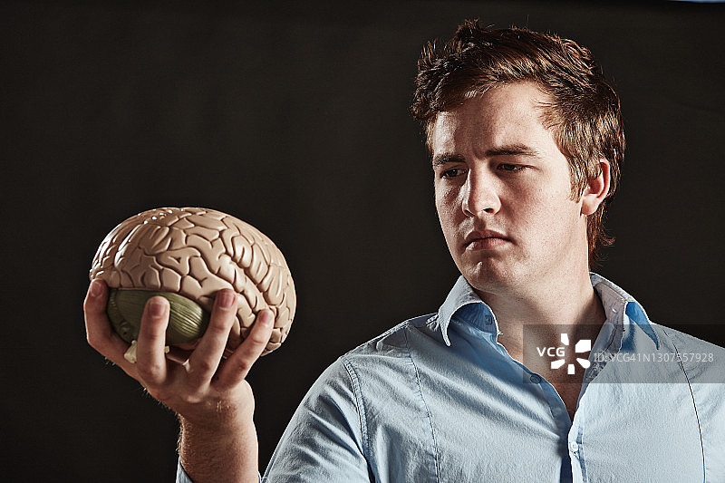 手持人脑、表情严肃坚定的年轻男子图片素材