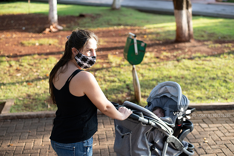 母亲戴着防护面具用婴儿车带着儿子。图片素材