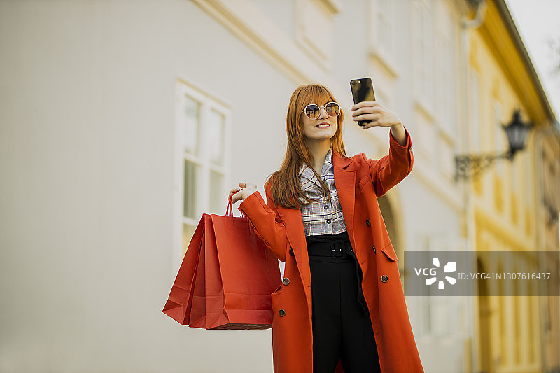 红发女孩提着购物袋在城市里进行视频通话图片素材