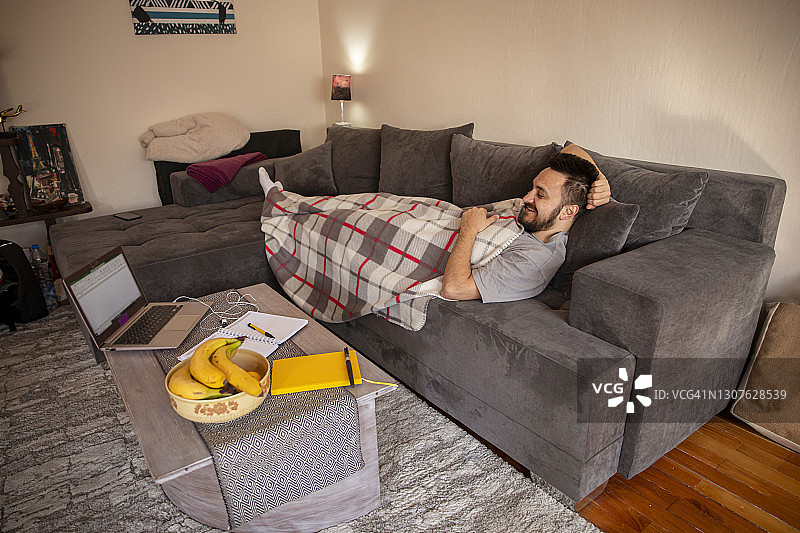 躺在沙发上用笔记本电脑进行视频通话的年轻男人图片素材