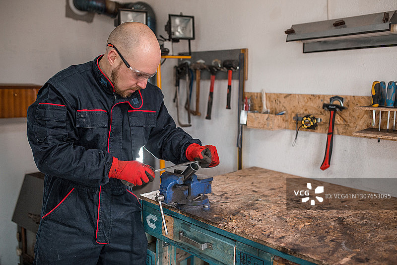 在小型金属车间使用手动工具的年轻工人图片素材