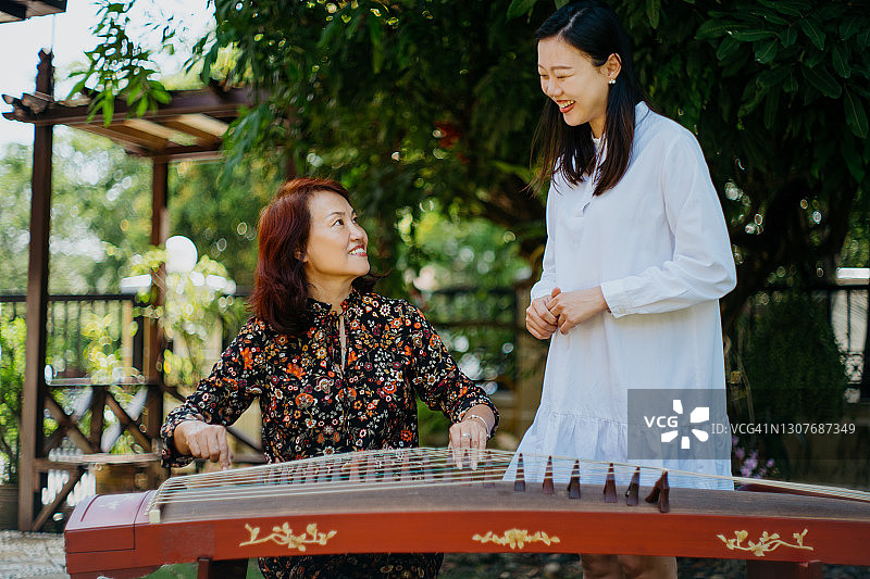 年轻的亚洲女性在母亲的指导下学习古筝图片素材