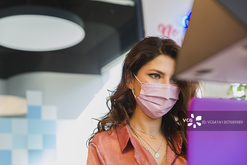 疫情期间，年轻女商人戴着口罩坐在办公室里，用笔记本电脑工作图片素材