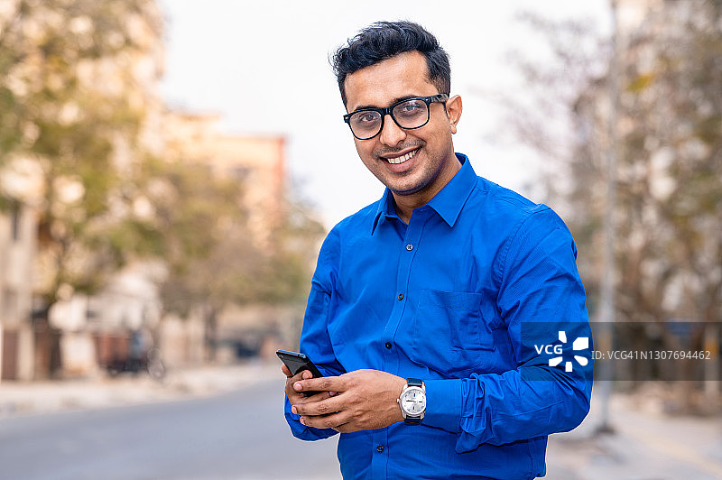 戴眼镜的商人手持智能手机的肖像图片素材