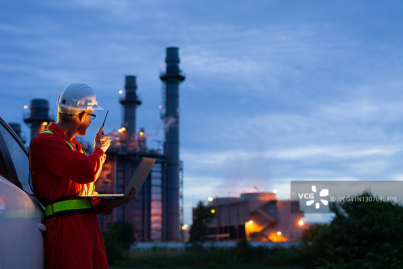 工程师戴安全帽在电厂背景下使用笔记本电脑图片素材