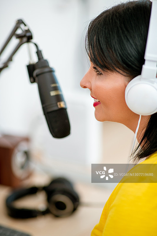 戴着耳机在麦克风前微笑的播客女人图片素材