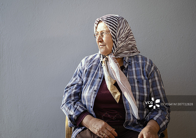 戴着头巾的中年穆斯林妇女，她坐在灰色墙前，土耳其穆拉图片素材