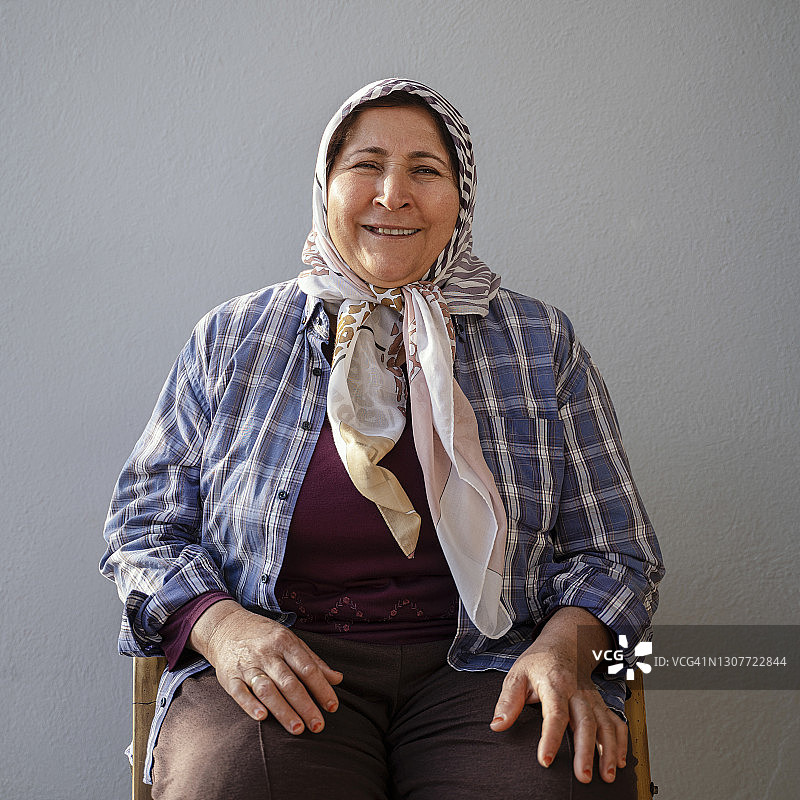 戴着头巾的中年穆斯林妇女，她坐在灰色墙前，土耳其穆拉图片素材