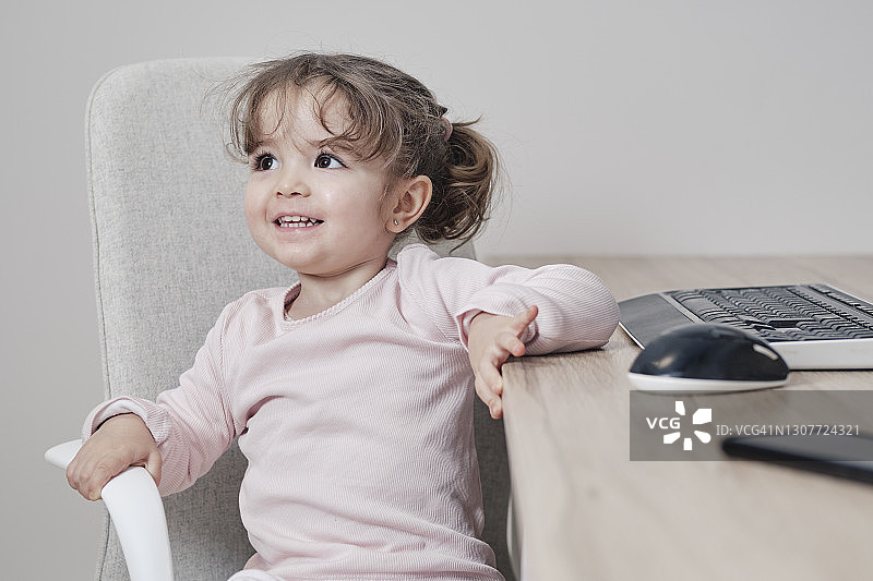 两岁女童高兴地坐在带键盘的办公椅上图片素材