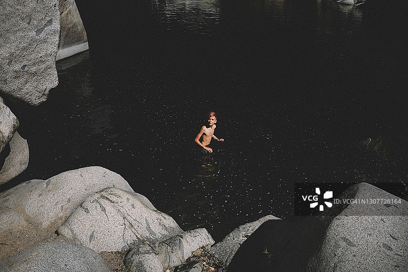 站在黑暗水中的粉红色头发男孩的远景镜头图片素材