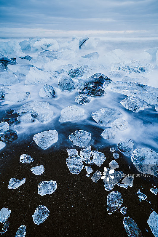 黑沙滩上冰块间流水的长曝光图片素材