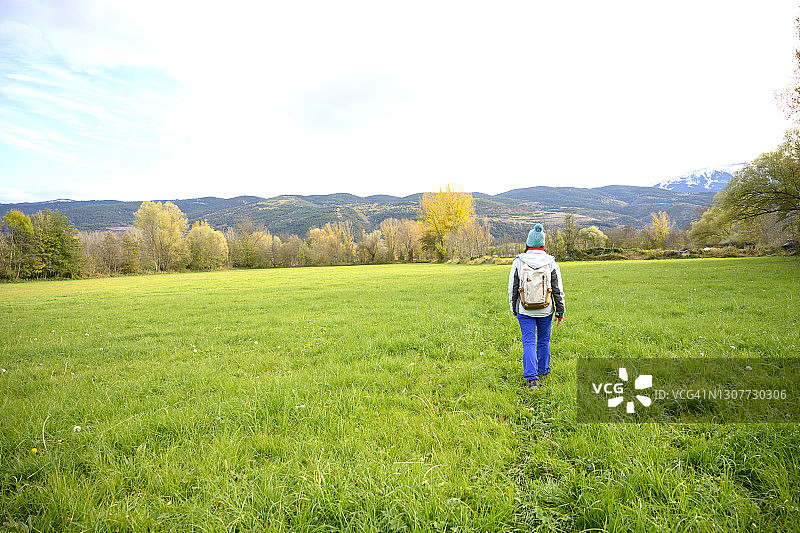 在绿色草地上行走的背包女人的背影图片素材