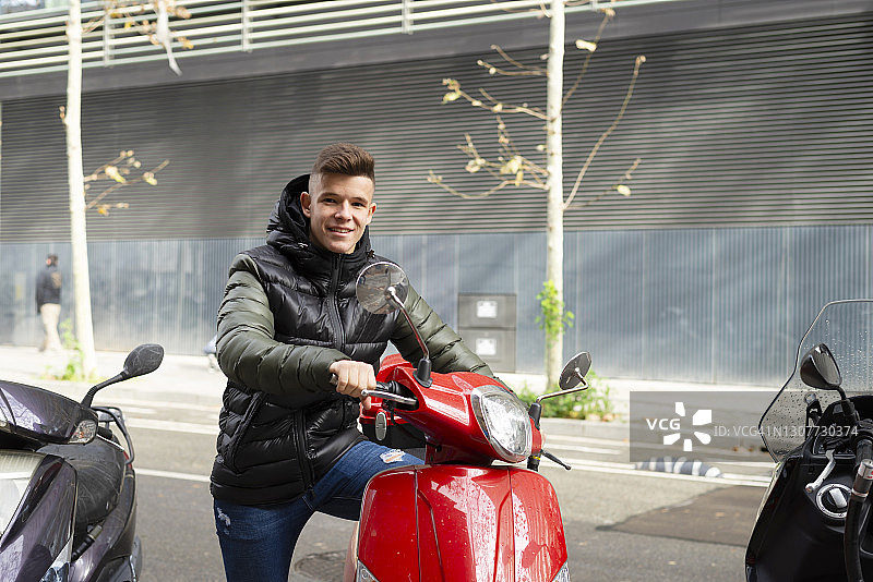 穿着时尚复古服装坐在滑板车上的年轻男人，看着镜头图片素材