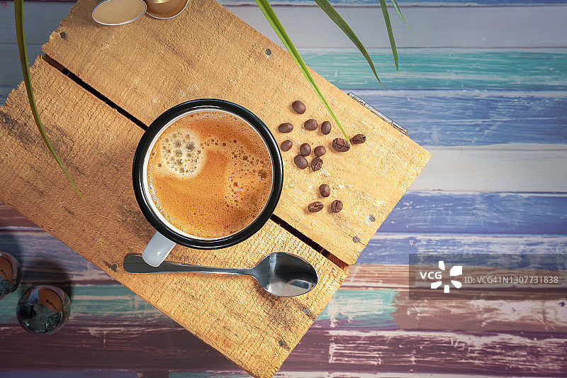 放在彩色木质表面的奶油咖啡白杯，旁边有咖啡豆图片素材