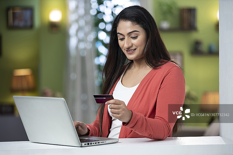 快乐的年轻女人在家用笔记本电脑进行网上购物的照片图片素材