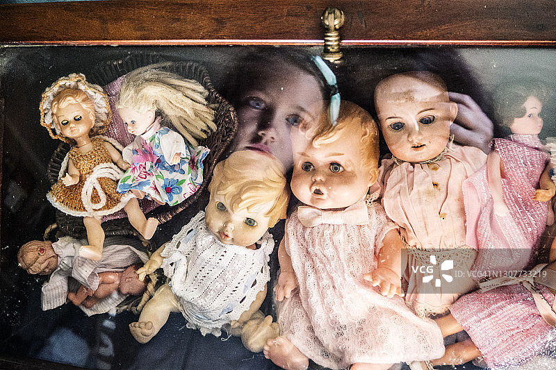 女孩看着装满娃娃的柜子的倒影图片素材