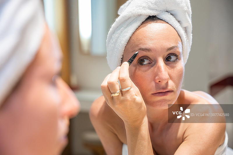 头发上裹着毛巾的女人拔眉毛的倒影图片素材