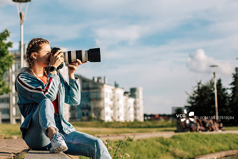 年轻女摄影师在街上户外工作，坐在草地上拍照图片素材