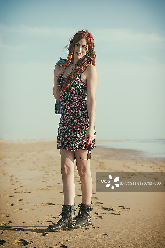 穿着连衣裙和靴子走在沙滩上的年轻女人图片素材
