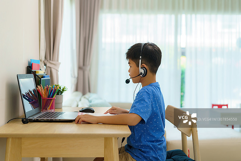 疫情期间在家通过笔记本电脑与老师在线学习数学的亚洲男孩图片素材