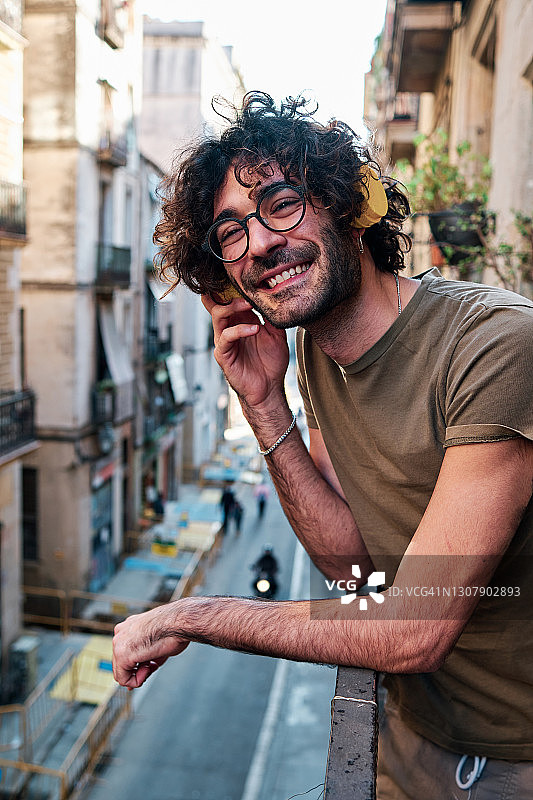 一个卷发年轻人在阳台上戴着耳机微笑图片素材