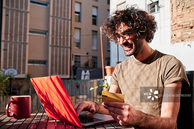 年轻男人在家中阳光明媚的一天用信用卡和笔记本电脑在线购物图片素材
