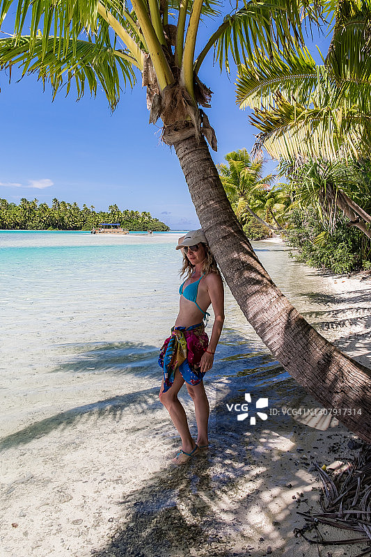 女子站在艾图塔基泻湖的独脚岛的棕榈树上，沐浴在阳光下图片素材