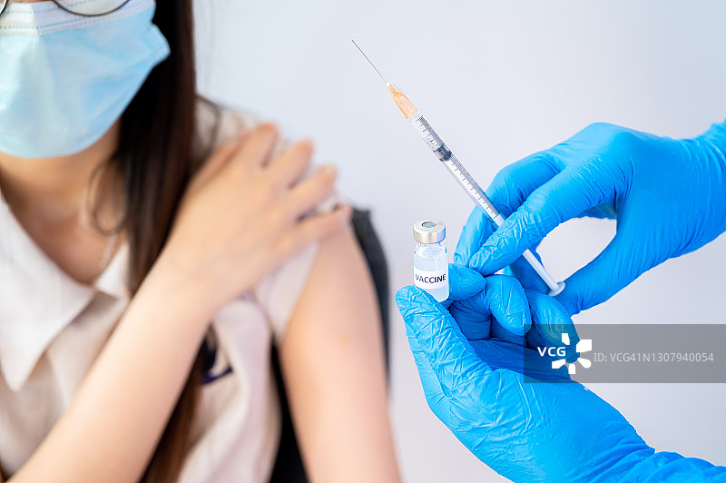 医生手持新冠疫苗和注射器，准备给女病人注射的特写图片素材