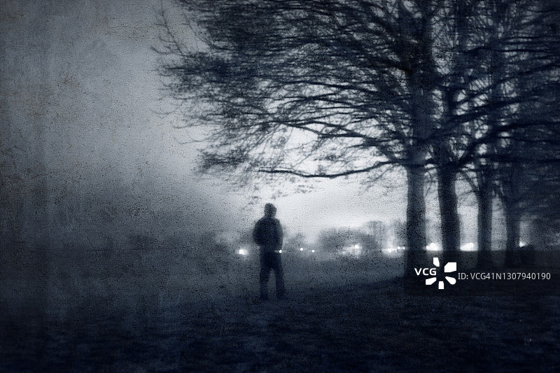 兜帽人站在城镇边缘的树旁，在一个怪异的雾夜，带有复古的颓废感图片素材