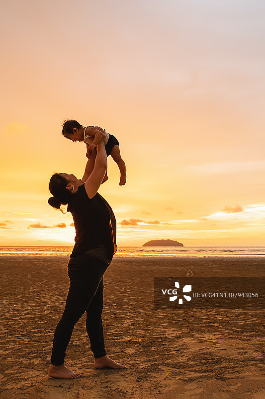 日落沙滩快乐母亲举起婴儿图片素材