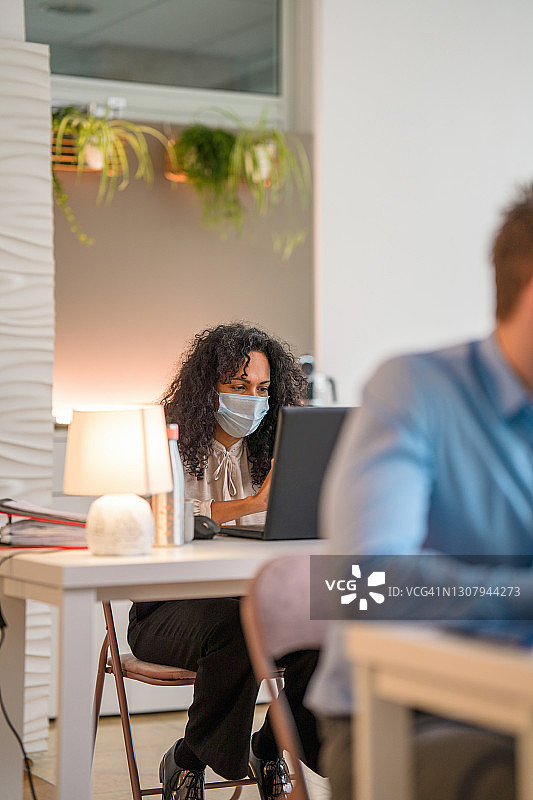 戴着口罩在办公室工作的西班牙裔中年女商人图片素材