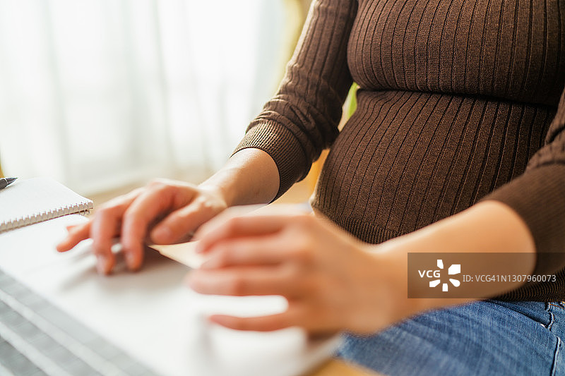 年轻孕妇在家中客厅用笔记本电脑工作图片素材