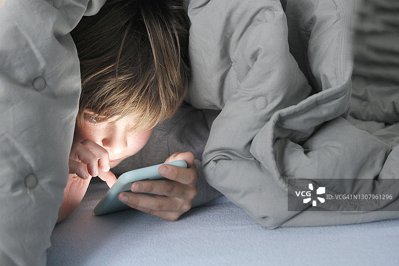 男孩在被窝里使用智能手机图片素材